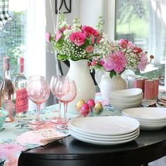 the table is set with plates, wine glasses and vases filled with pink flowers