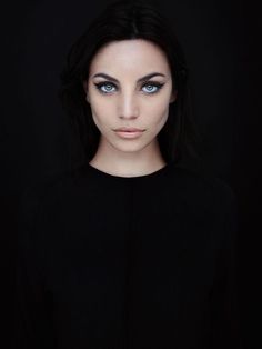 a woman with long black hair and blue eyes is posing for the camera in front of a dark background