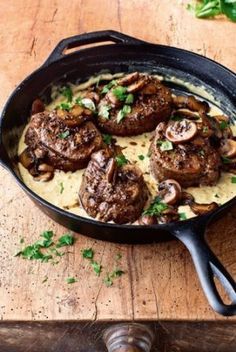 a skillet filled with meat and mushrooms on top of a wooden table