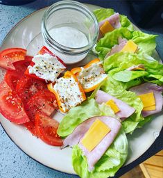 a white plate topped with lettuce and tomatoes next to a jar of dressing