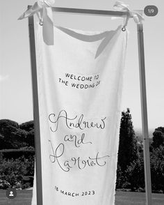 a welcome sign hanging from a pole in front of a field with trees and bushes