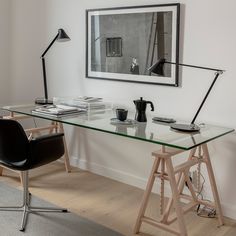 a glass desk with two chairs in front of it and a framed photograph on the wall