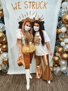 two young women standing next to each other in front of a backdrop with gold balloons