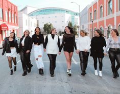 a group of women are walking down the street in black and white outfits, all smiling