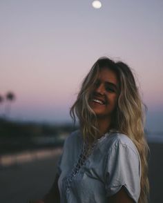 black and white photo of smiling woman in the evening with full moon behind her head