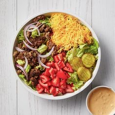 a salad with meat, cheese and tomatoes in a bowl next to a cup of coffee