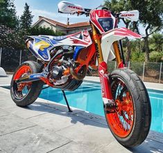 a red, white and blue dirt bike parked next to a swimming pool