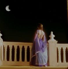 a woman in a purple sari is standing on a balcony looking at the moon