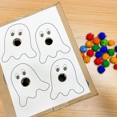 a cardboard box with three ghost faces cut out and colored pom poms around it