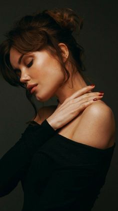 a woman with her hand on her shoulder posing for the camera, wearing a black top