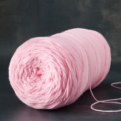 a skein of pink yarn sitting on top of a black table next to a ball of thread