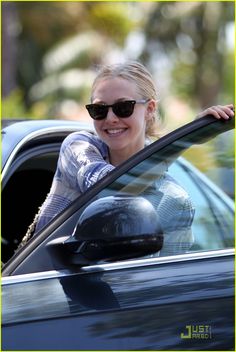 a woman in sunglasses is sitting in a car with her hand out the window and smiling