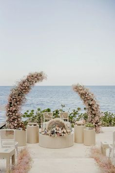 an outdoor wedding setup with flowers on the arch and water in the backround