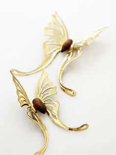 two gold metal wall hangings with wood beads and leaves on the ends, one is shaped like a butterfly