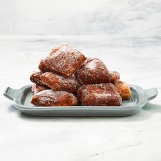 a pile of powdered sugar donuts sitting on a gray platter next to a marble counter top