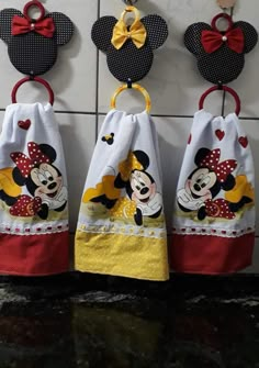 three mickey mouse towels hanging from hooks on the wall in front of a tiled wall