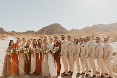 a group of people standing next to each other in front of some mountains and sand