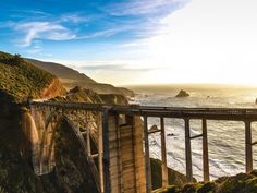 the sun is setting over the ocean and a bridge that goes to the top of a cliff