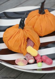 two small pumpkins sitting on top of a white and black plate with candy candies