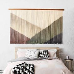 a bed with pillows and blankets on it in front of a wall hanging over the headboard