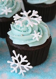 cupcakes with frosting and snowflakes on them are sitting on a table