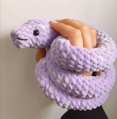 a hand is holding a purple knitted snake toy in the shape of a scarf