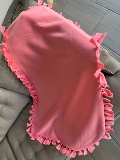 a pink blanket with ruffles on it sitting on top of a gray couch