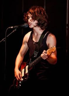 a young man playing an electric guitar in front of a microphone