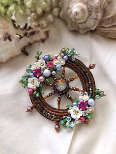 a close up of a brooch on a white cloth with beads and flowers in it