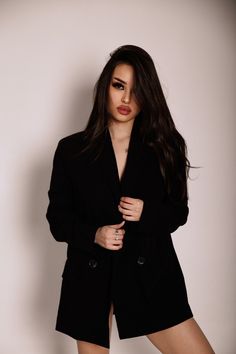 a woman posing for the camera wearing a black coat and high heels with her hands on her hips