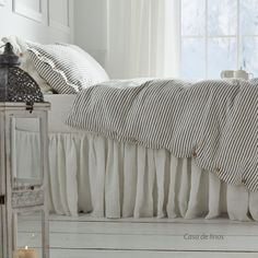 a white bed sitting next to a window in a room with curtains on the windowsill