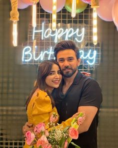 a man and woman hugging each other in front of a neon sign that says happy birthday