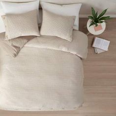 a bed with two pillows and a plant on the floor next to it in front of a white wall