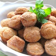 a white bowl filled with sugared pastries covered in powdered sugar and garnished with a green leaf