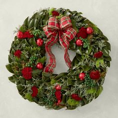 a christmas wreath hanging on the wall with red berries and greenery in front of it