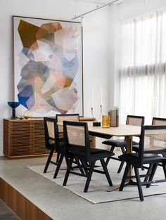 a dining room table and chairs in front of a large abstract painting on the wall