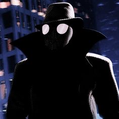 a man in a black suit and hat standing next to a tall building at night