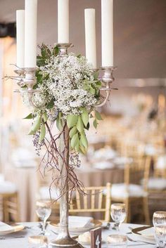 an elegant centerpiece with white flowers and greenery is displayed on a silver candelabra