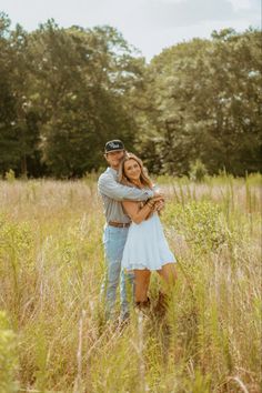 a man and woman are hugging in the tall grass with trees in the back ground