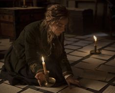 a woman kneeling on the floor holding a candle in her hand and looking down at it