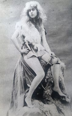 an old fashion photo of a woman with long hair and stockings sitting on a rock