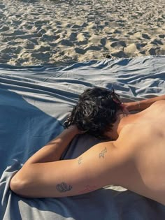 a man laying on top of a beach covered in a blanket next to the ocean