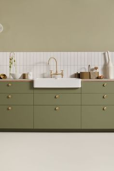 a kitchen with green cabinets and white tiles on the wall, along with gold handles