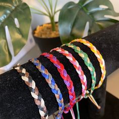 four different colored braided bracelets sitting on top of a black piece of cloth