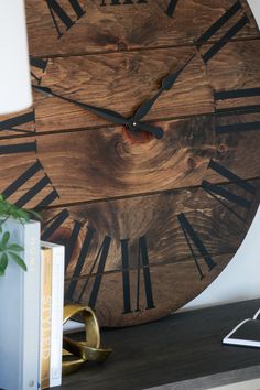 a large wooden clock sitting on top of a table next to a book and lamp