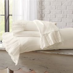 a bed with white sheets and pillows on top of it next to a brick wall