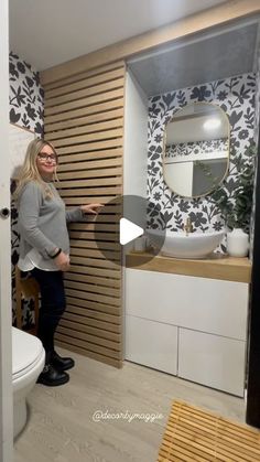 a woman standing in front of a bathroom mirror next to a white toilet and sink