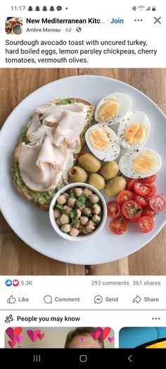 a white plate topped with an open face sandwich next to sliced eggs and tomatoes on top of a wooden table