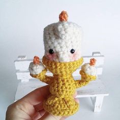 a small crocheted doll is posed on a bench with its arms in the air