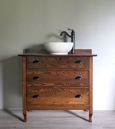 a bathroom sink sitting on top of a wooden dresser next to a wall mounted faucet